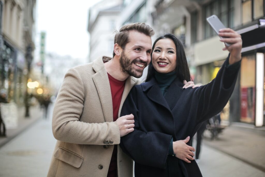 Man in Brown Coat Smiling Beside Woman in Black Coat Taking Selfie-Love Languages