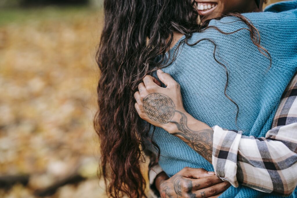 Unrecognizable African American tattooed person embracing anonymous girlfriend with dark hair during romantic date while standing in nature on autumn day-Flirting 