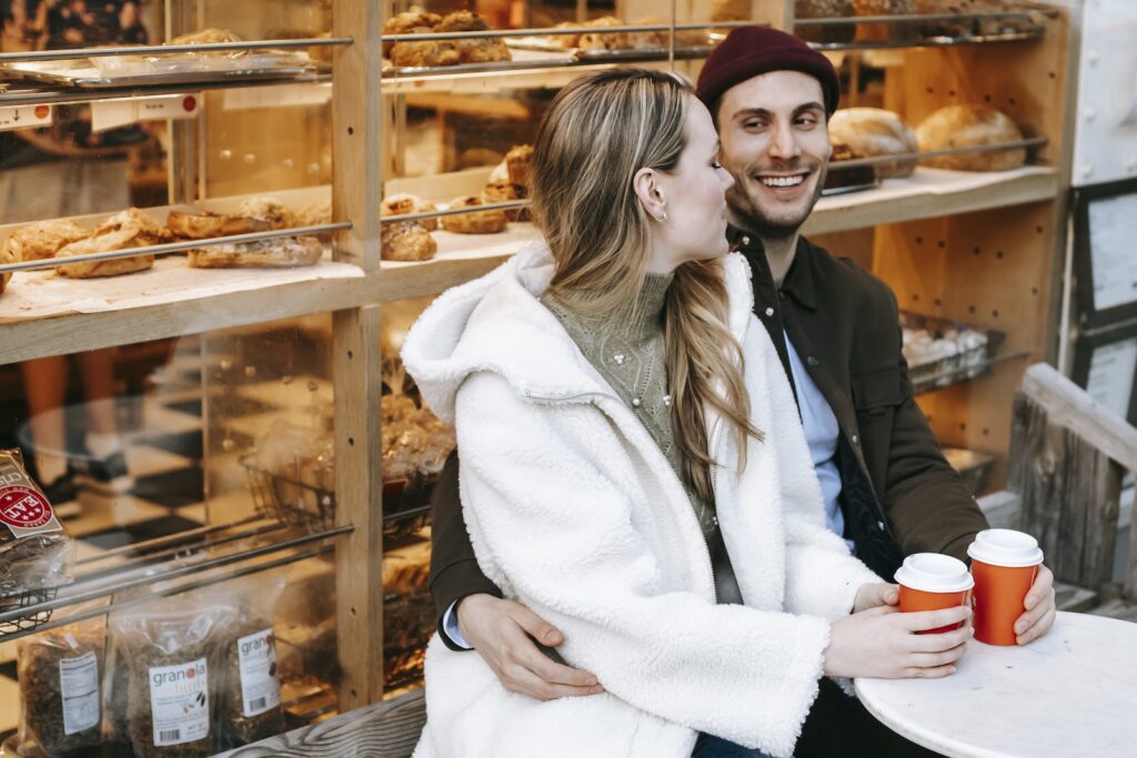 Cheerful young woman and man embracing in cafe having coffee in paper cups-Love and Appreciation