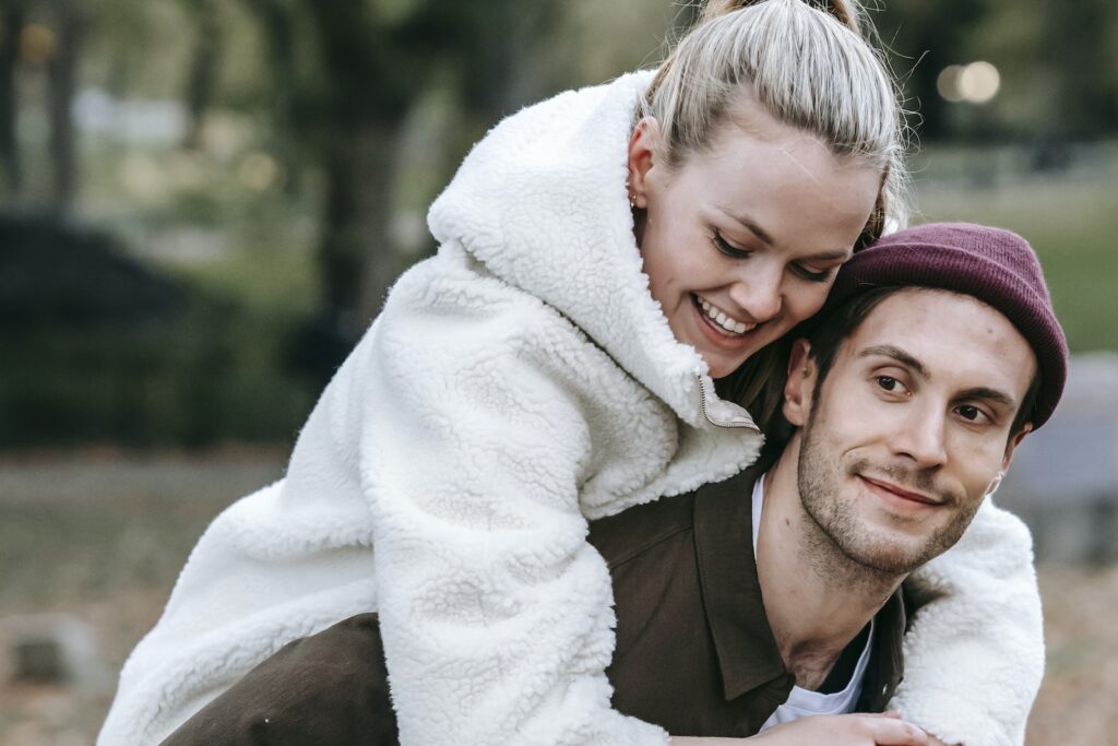 Smiling man giving piggyback ride to beloved woman in park-Flirting