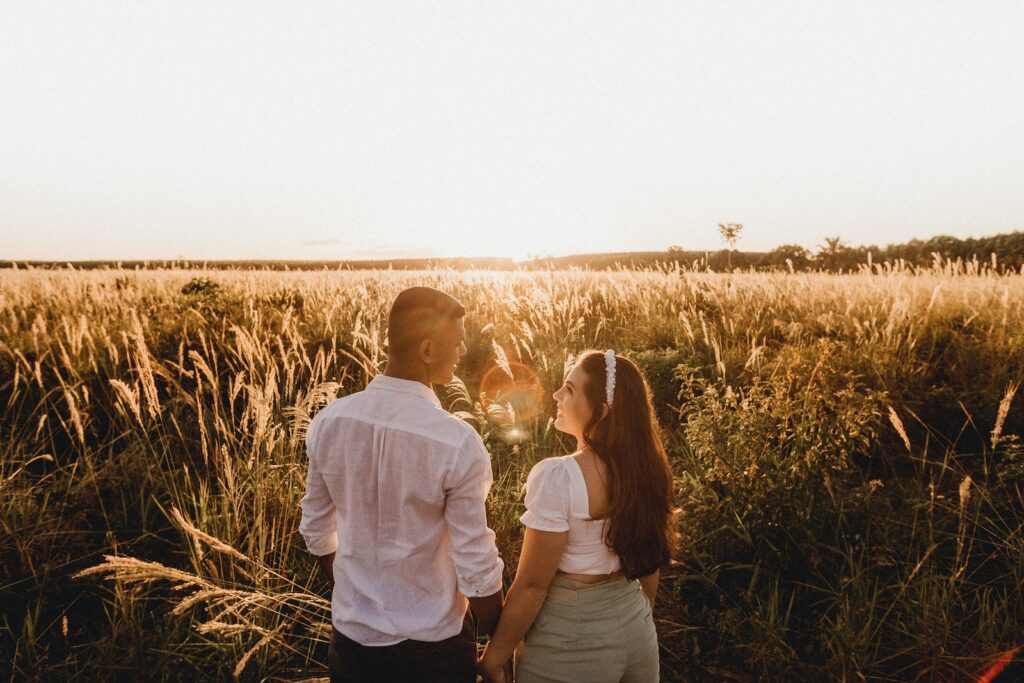High angle back view of diverse couple holding hands standing in meadow with cereal grass and looking at each other with love-Toxic Relationship