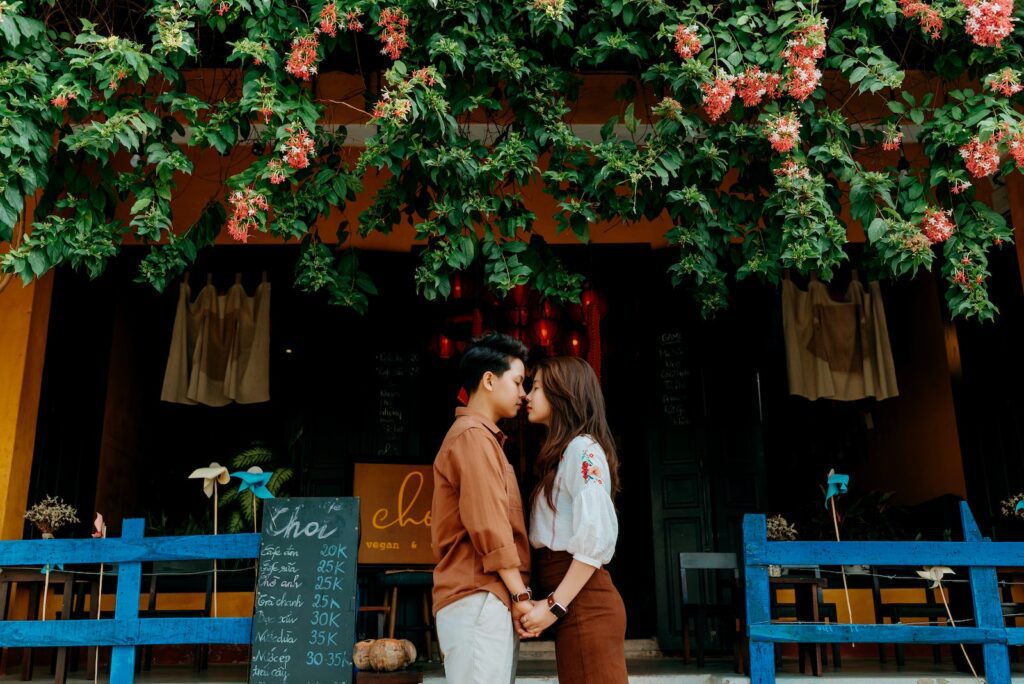 Side view of romantic young Asian couple in trendy clothes holding hands and touching noses while standing near entrance of cozy cafe in city-Successful People Fail in Love