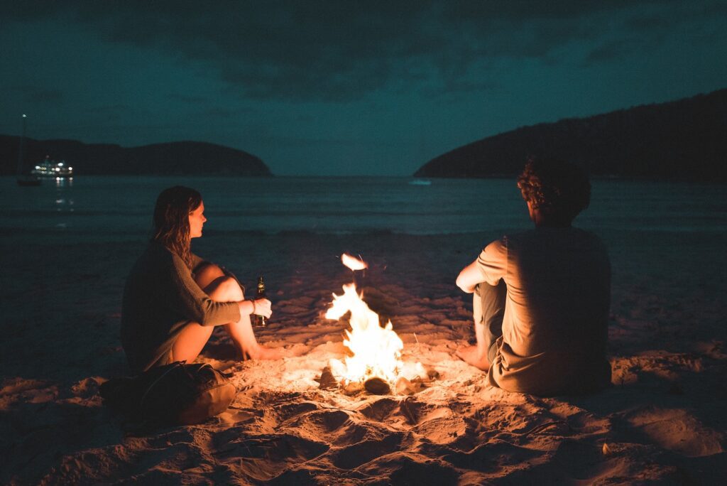 man and woman with bone fire sitting on seashore-love