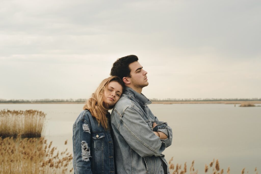 woman in blue denim jacket leaning on man's shoulder near body of water - Shared Experiences