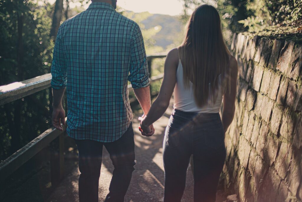 Back View Photo of Couple Holding Hands While Walking Along Pathway-Spark of Attraction