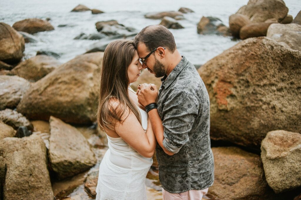 Photo of Couple Holding Each Other While Standing by Rocks Next to Body of Water-Passionate Marriage
