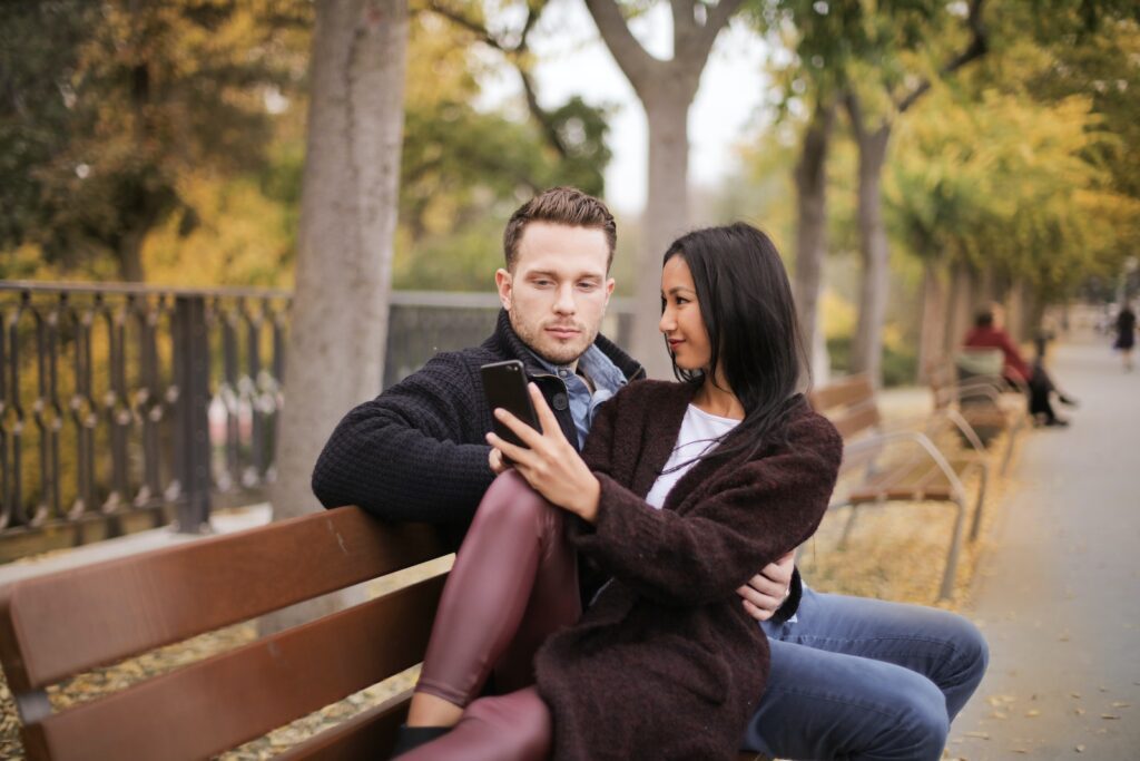 Selective Focus Photo of Couple Sitting on Brown Wooden Bench Looking at a Phone Friendzone 