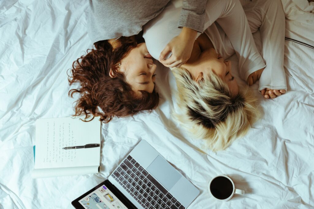 From above of young lesbian couple lying on bed and resting with laptop and cup of coffee while chilling on weekend together Relationship for Introverted Couples