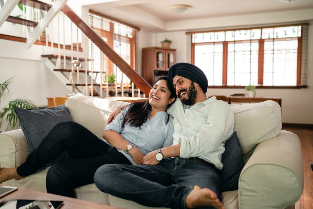 Happy young Indian couple laughing and cuddling while relaxing on couch-Dating Mistakes