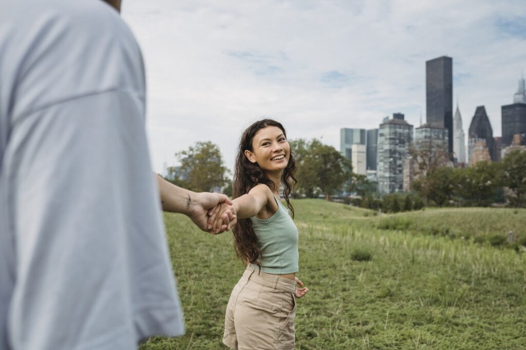 Crop anonymous man holding hand and following happy young ethnic girlfriend while spending time together in green park in New York Relationship for Introverted Couples