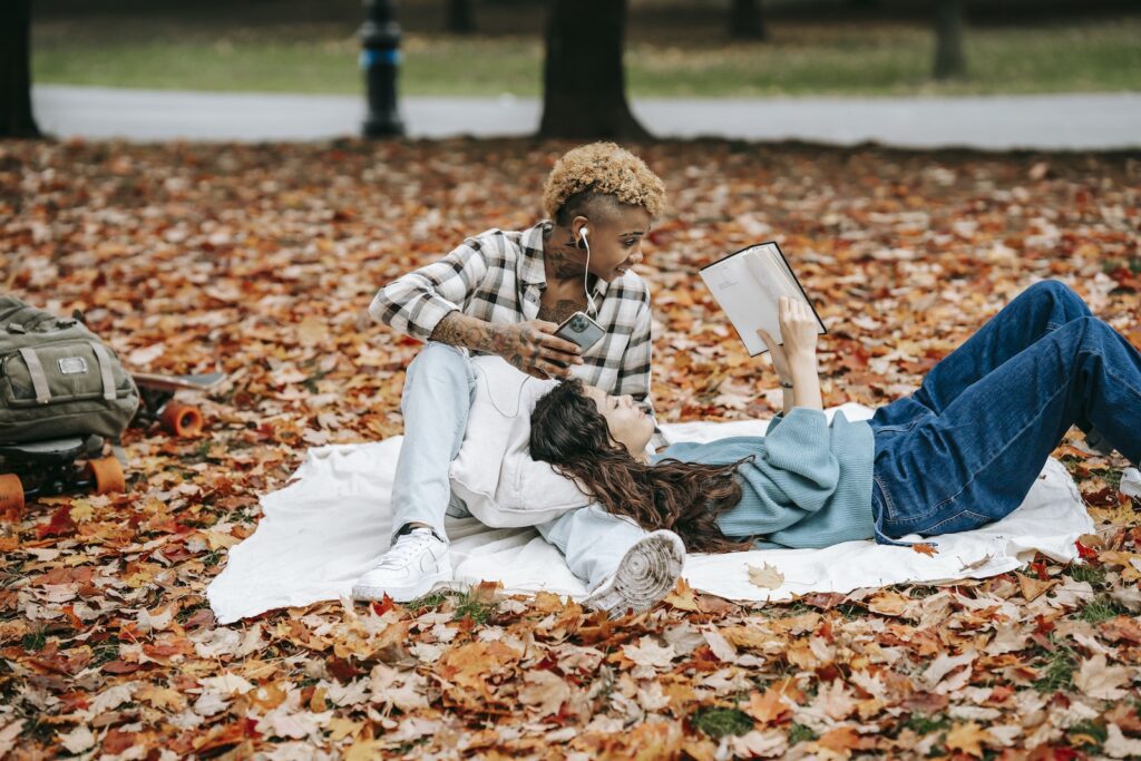 Focused Hispanic woman reading book while lying on lap of African American female listening to music during weekend together on autumn day Untamed Love