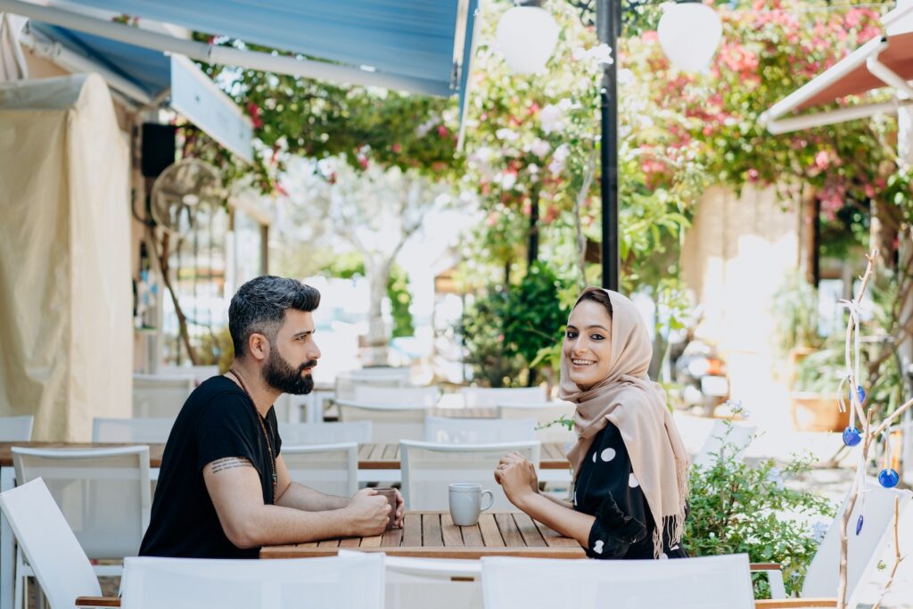 Man and Woman in Headscarf Drinking from Cups Outside Untamed Love
