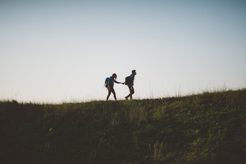 couple walking on hill while holding during daytime-Romantic Gestures
