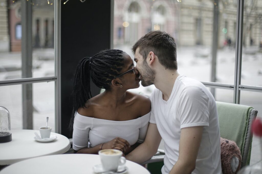 Happy young diverse couple kissing while resting at modern light cafe at table near window while having date and drinking hot coffee-Balancing Work and Marriage