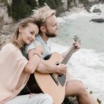 Cheerful romantic couple recreating on rocky cliff against sea with guitar Use Reverse Psychology and Make Him Desperately Chase You
