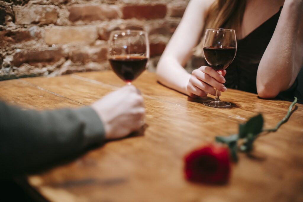 Crop anonymous couple in elegant outfits enjoying romantic date in bar at table with red rose and glasses with wine near brick wall-Healthy Sex