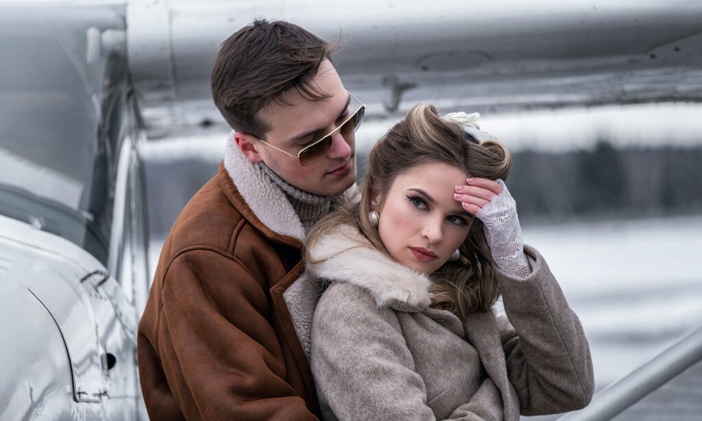 Side view young stylish couple in outerwear cuddling gently near modern propeller jet on snowy airfield-Make Him Want You More Than Just Sexually