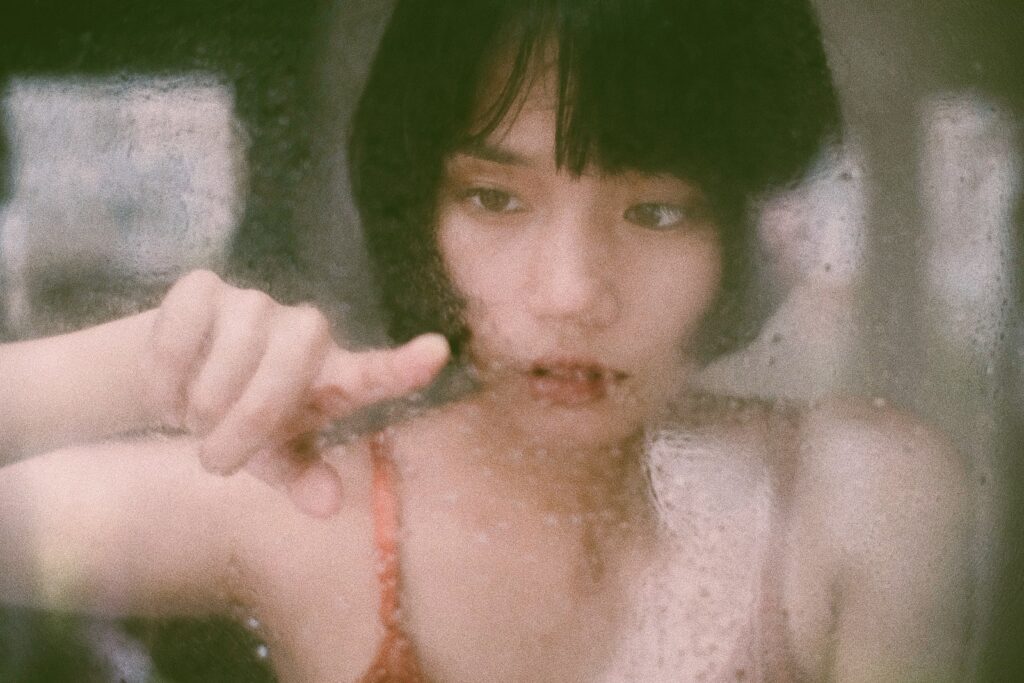 Through window of young Asian woman drawing on wet glass with finger in soft light-Red Flags