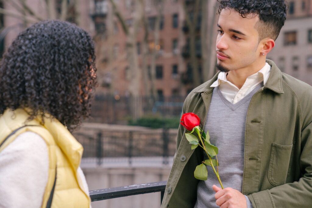 Crop romantic young Hispanic guy in casual clothes giving red rose to anonymous girlfriend with dark curly hair during romantic date on city street-Women Should Look for in a Partner
