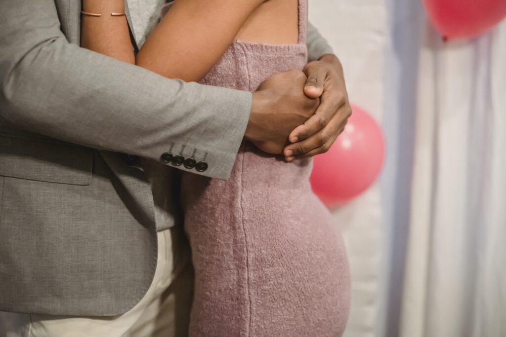 Side view of crop faceless black couple in elegant clothes standing in bright room and cuddling while dancing together near pink balloons on wall and curtains-Quality Time in Relationships