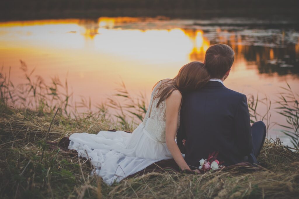 Wedding Couple Sitting on Green Grass in Front of Body of Water at Sunset-Financial Harmony
