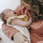 Side view of crop anonymous mother consoling crying infant baby in arms while sitting in light room near wall at home Financial Advice for Marriage Breakup