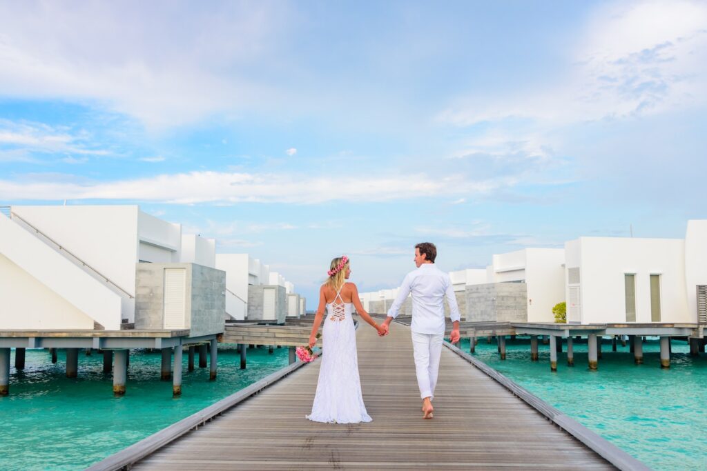 Full body back view of unrecognizable loving couple in white clothes walking on boardwalk above water near buildings while holding hands and looking at each other-Good Morning Messages for Him That Touch the Heart